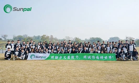 Large Sunpal team posed outdoors on a grassy field holding a long green banner, smiling for a group photo.